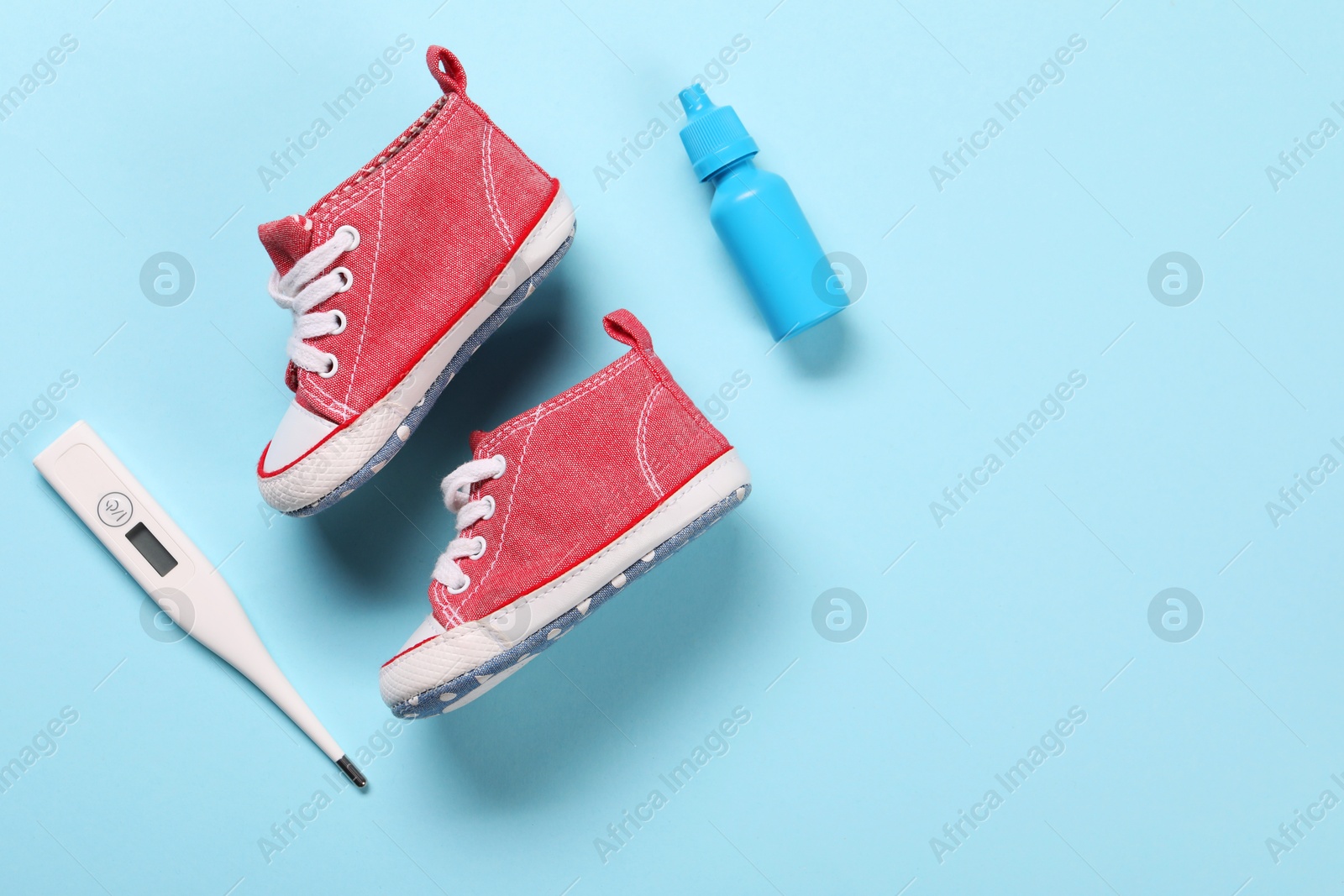 Photo of Kid's sneakers, thermometer and nasal spray on light blue background, flat lay. Space for text