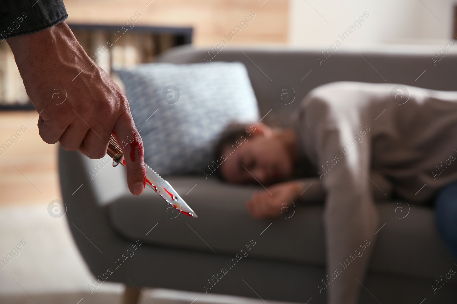 Photo of Man with bloody knife and his victim on couch indoors, closeup. Dangerous criminal