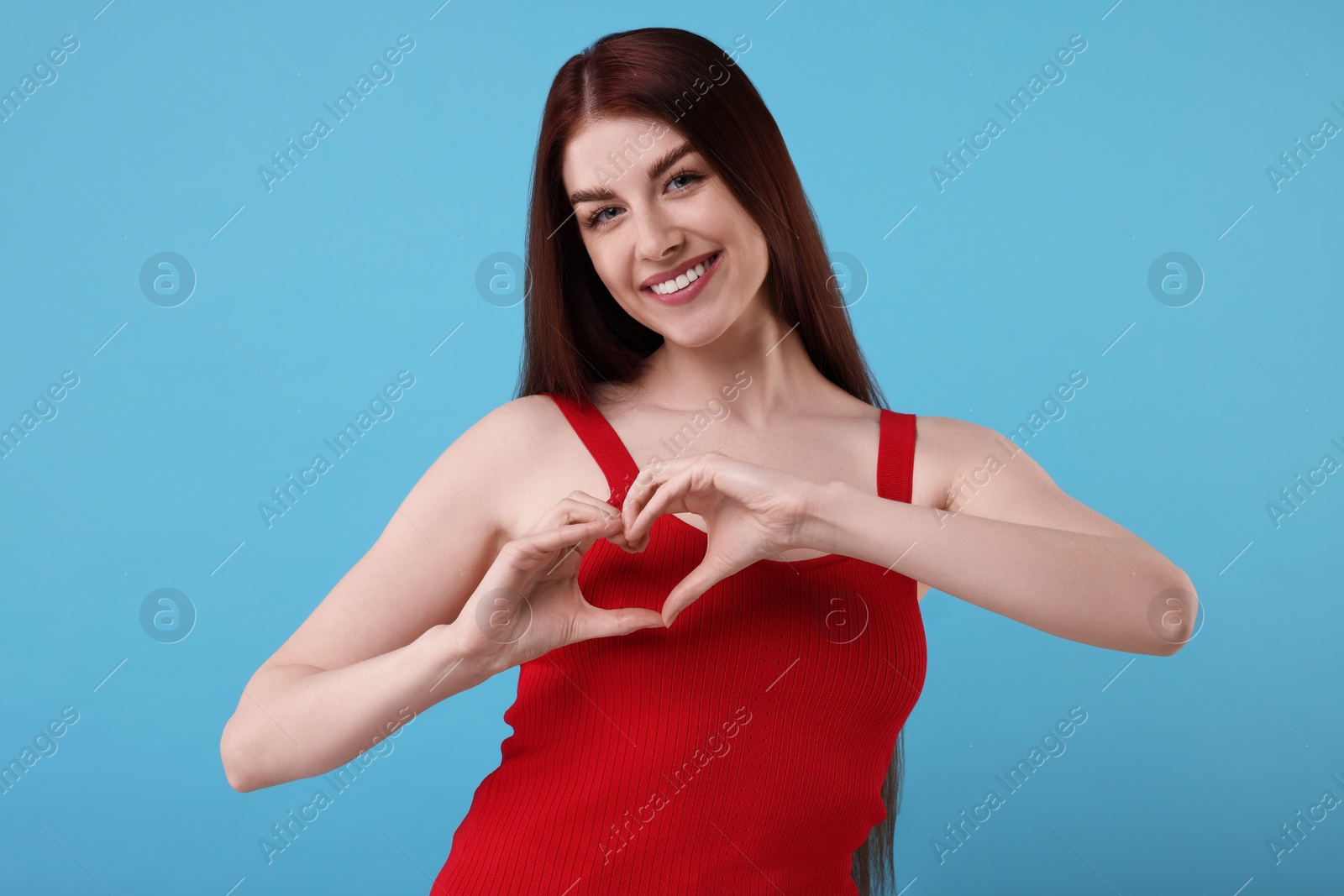 Photo of Happy young woman showing heart gesture with hands on light blue background