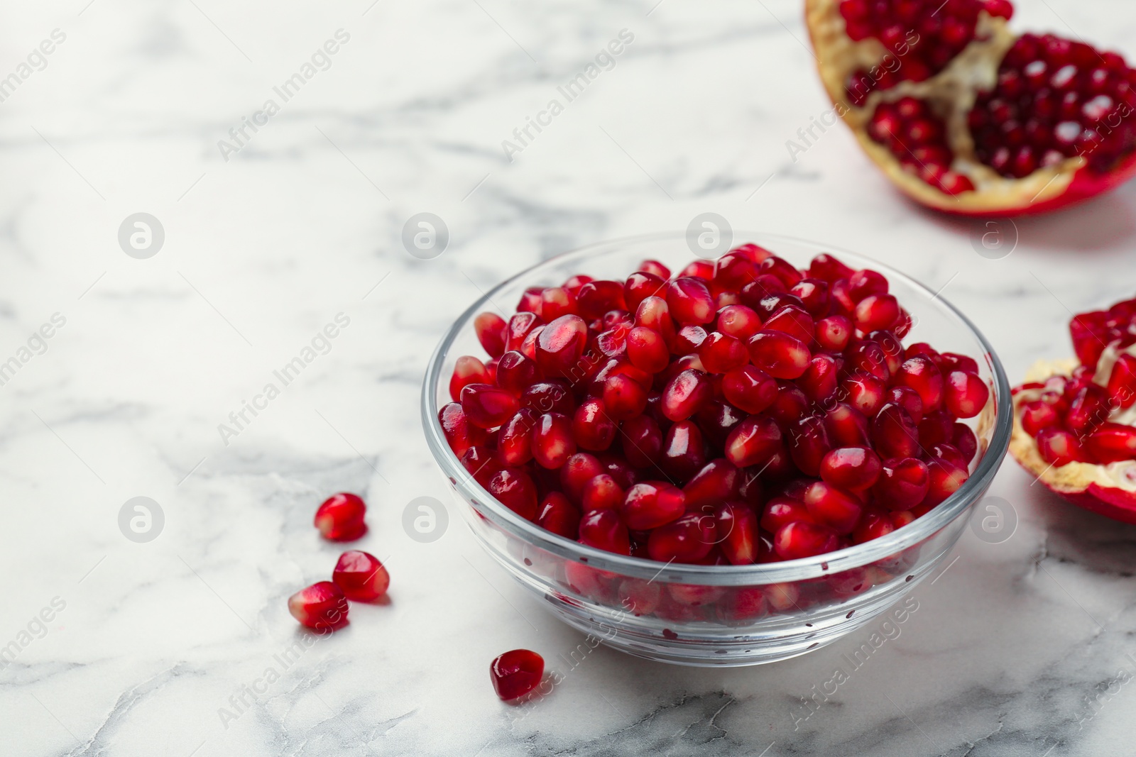 Photo of Ripe juicy pomegranate grains in bowl on white marble table, space for text