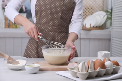 Photo of Woman making dough with whisk in bowl at table, closeup