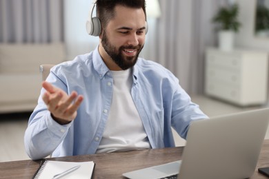 Young man in headphones using video chat during webinar at table in room