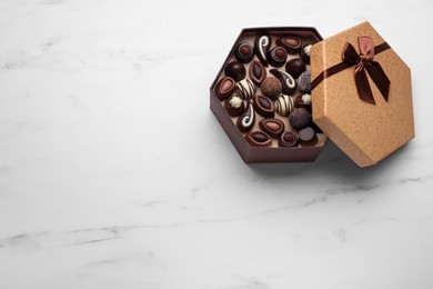 Open box of delicious chocolate candies on white marble table, top view. Space for text