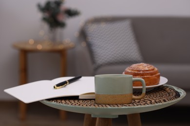 Cup of drink, pastry and notebook on coffee table indoors