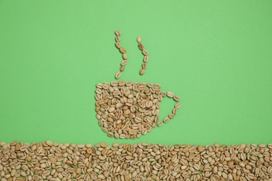 Cup of hot drink, composition made with coffee beans on green background, flat lay