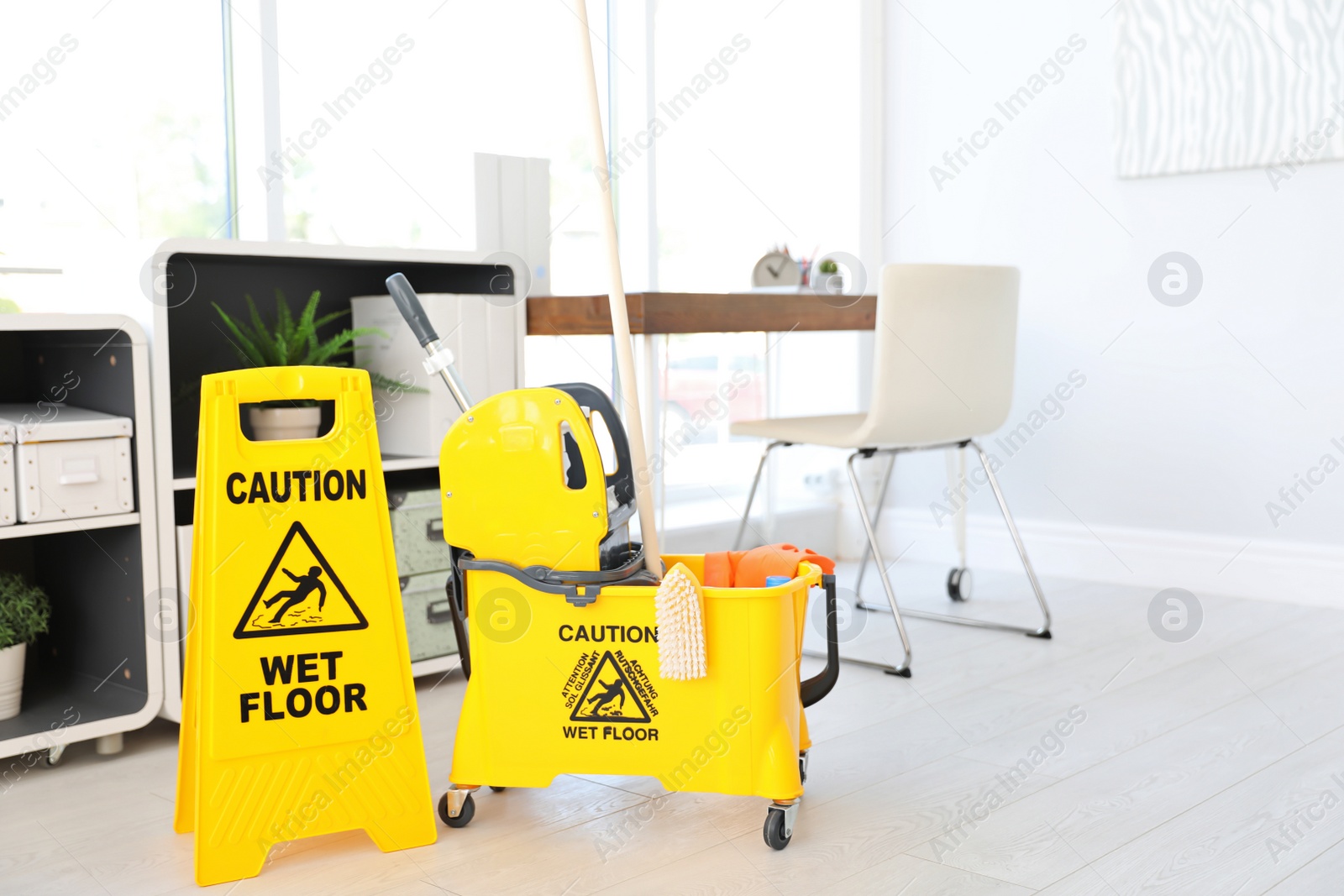 Photo of Phrase "CAUTION WET FLOOR" on safety sign and mop bucket with cleaning supplies, indoors