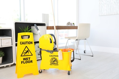 Photo of Phrase "CAUTION WET FLOOR" on safety sign and mop bucket with cleaning supplies, indoors