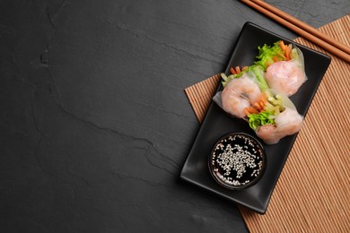 Photo of Tasty spring rolls served with soy sauce on dark grey textured table, flat lay. Space for text