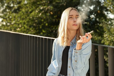 Photo of Woman smoking cigarette near railing outdoors. Space for text