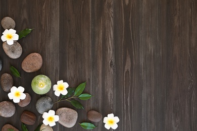 Flat lay composition with spa stones, flowers and candle on wooden background. Space for text