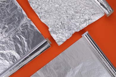 Photo of Different rolls of aluminum foil on orange background, flat lay