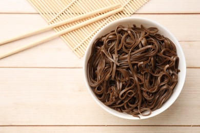 Photo of Tasty buckwheat noodles (soba) with chopsticks on wooden table, flat lay. Space for text