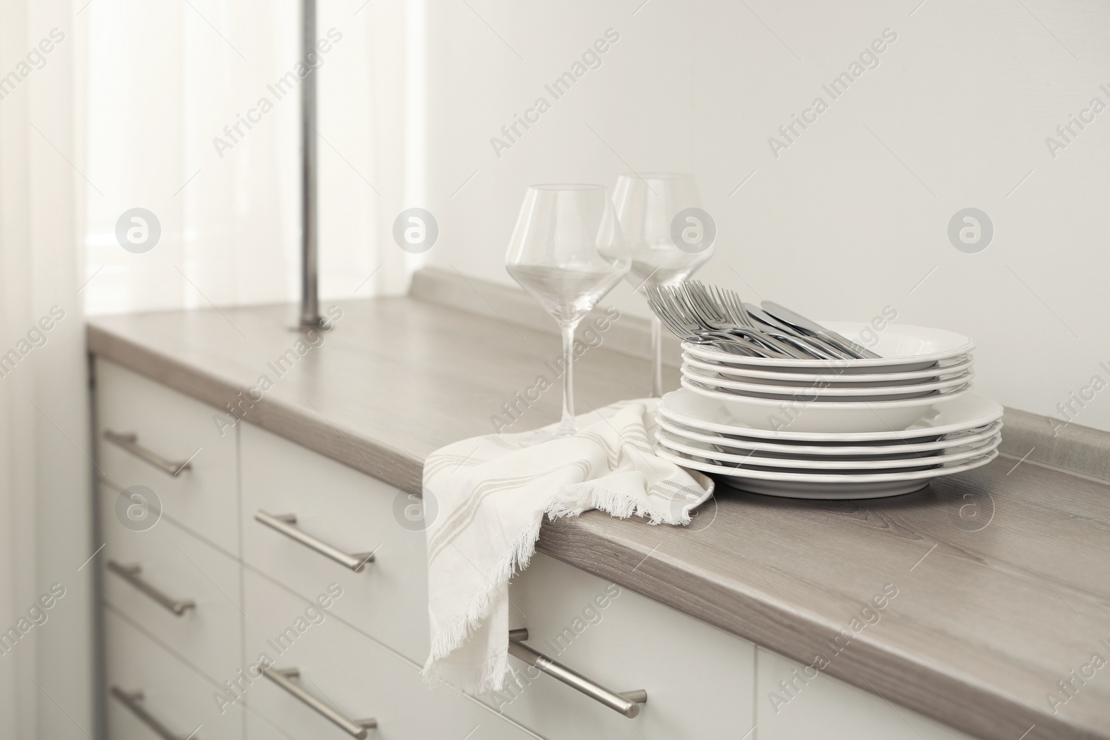 Photo of Clean dishware, cutlery and wineglasses on chest of drawers indoors