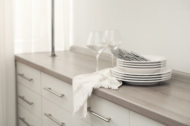 Photo of Clean dishware, cutlery and wineglasses on chest of drawers indoors