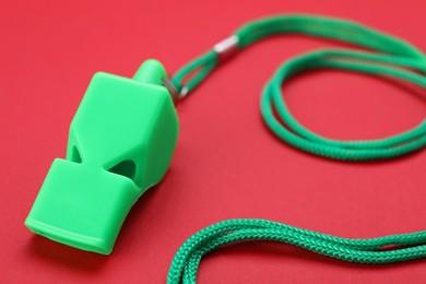 Photo of One green whistle with cord on red background, closeup