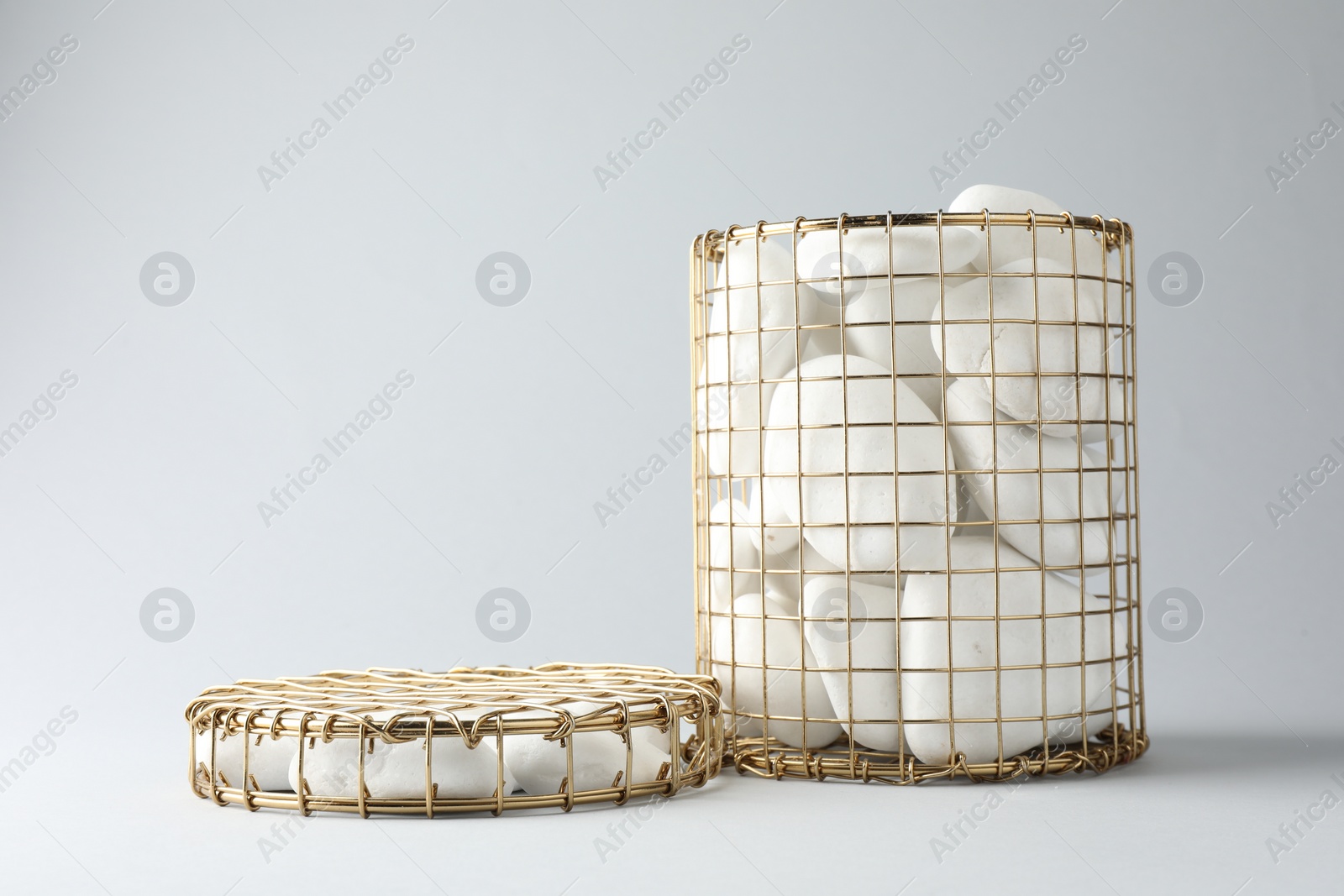 Photo of Presentation for product. Podiums made of pebbles and wire basket on light grey background. Space for text