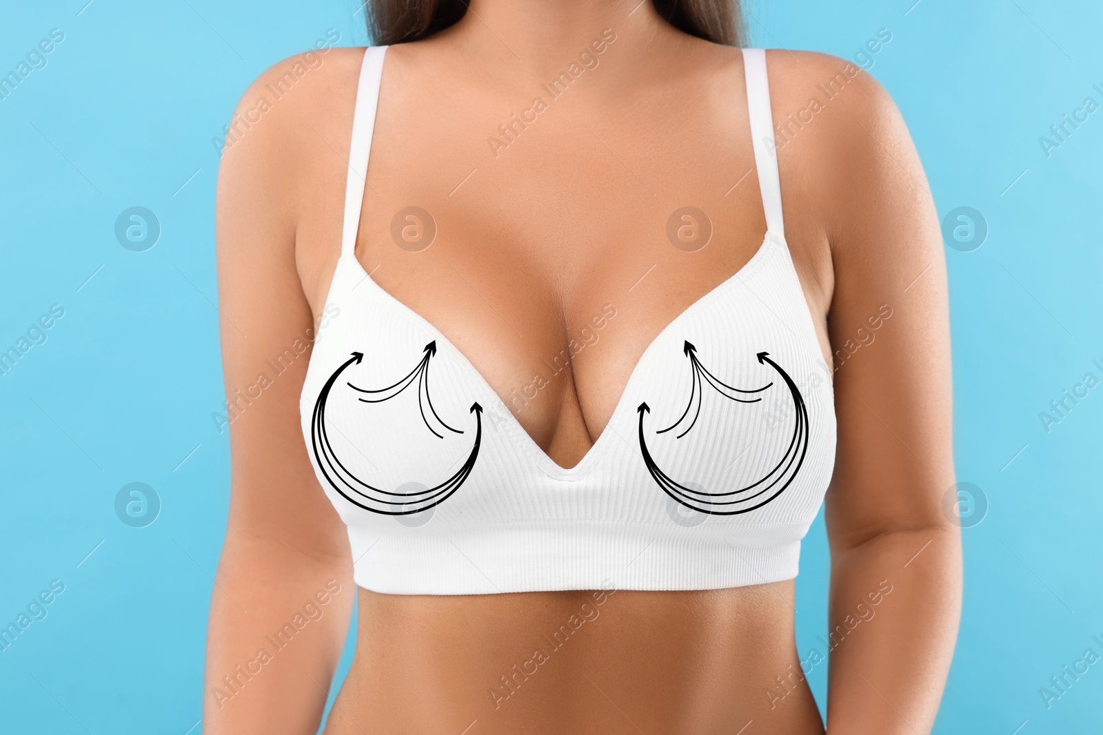 Image of Breast surgery. Woman with markings on bra against light blue background, closeup