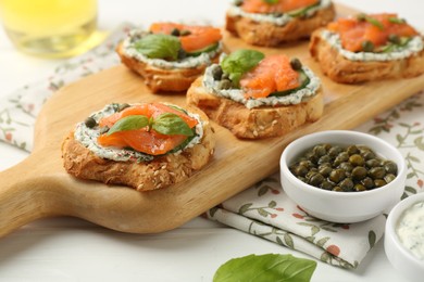 Tasty canapes with salmon, capers, cucumber and sauce on white wooden table, closeup