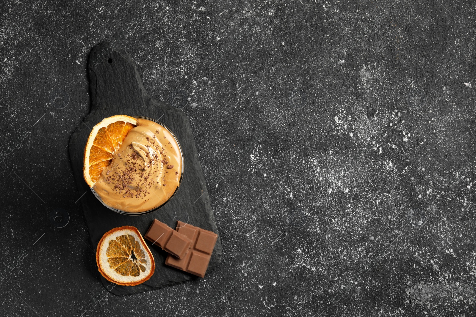 Photo of Glass of delicious dalgona coffee with dry orange and chocolate on grey textured table, top view. Space for text