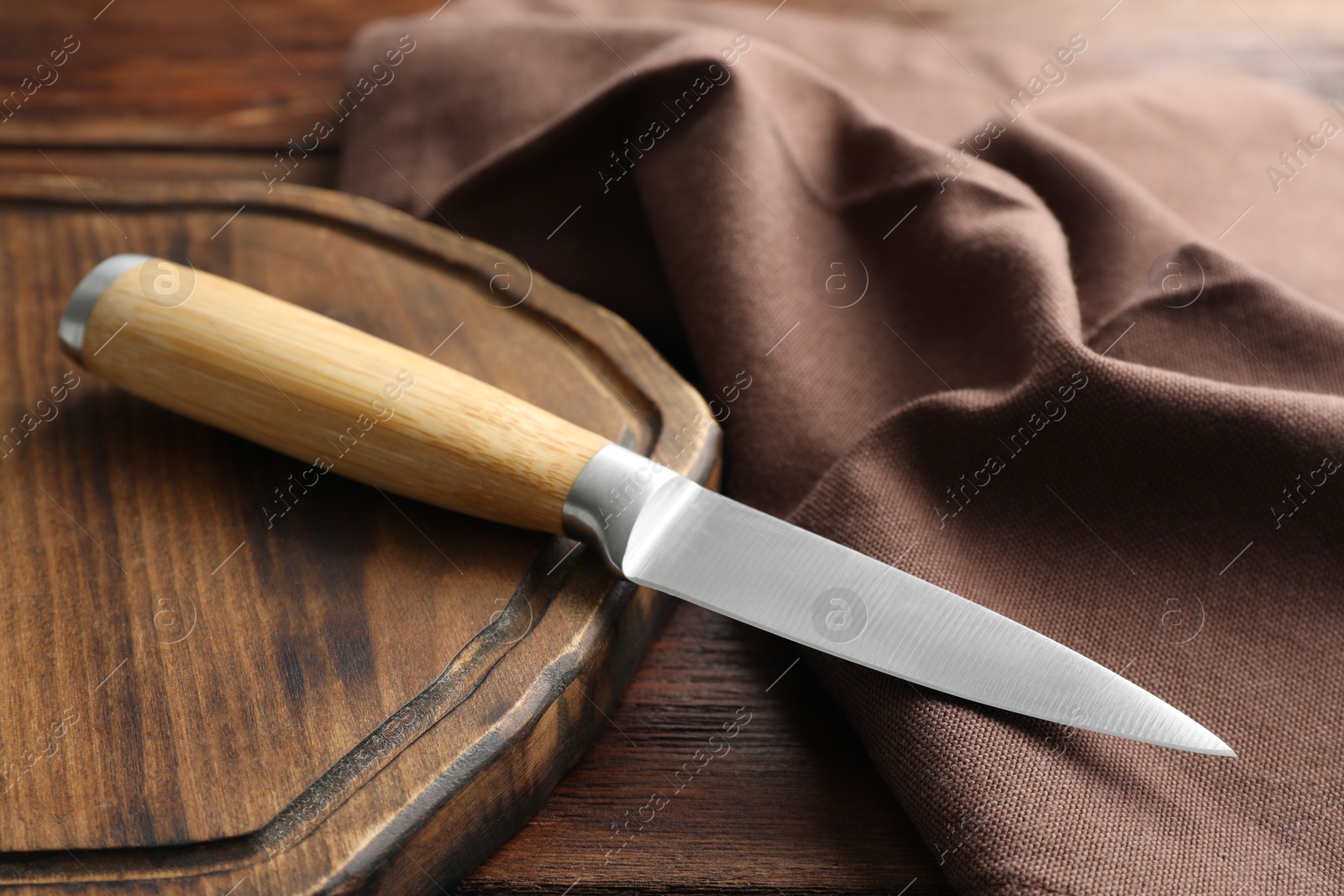 Photo of One sharp knife, cloth and board on wooden table, closeup