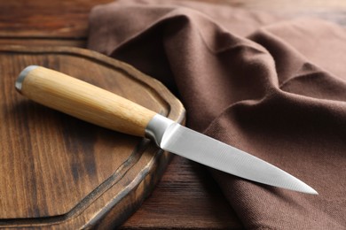 Photo of One sharp knife, cloth and board on wooden table, closeup