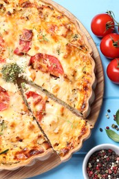 Photo of Tasty quiche with tomatoes, microgreens and cheese served on light blue wooden table, flat lay