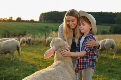Photo of Mother and son stroking sheep on pasture. Farm animals