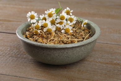 Dry and fresh chamomile flowers in bowl on wooden table, closeup