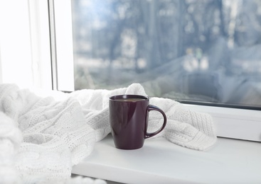 Cup of winter drink and knitted scarf on windowsill. Space for text