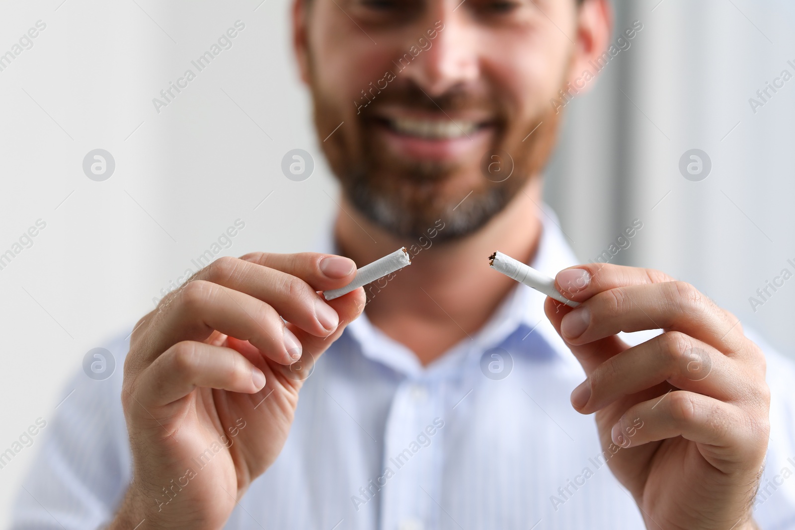 Photo of Stop smoking concept. Man holding pieces of broken cigarette on light background, closeup