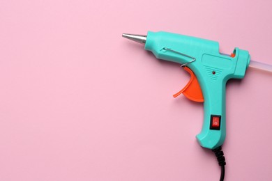Photo of Turquoise glue gun with stick on pink background, top view. Space for text