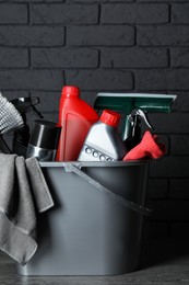 Photo of Different car cleaning products in bucket near black brick wall