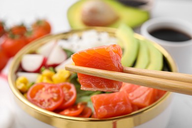 Chopsticks with salmon over delicious poke bowl, closeup