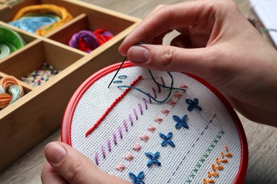 Photo of Woman doing different stitches with colorful threads on fabric in embroidery hoop at wooden table, closeup