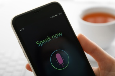 Photo of Woman using voice search on smartphone against blurred background, closeup