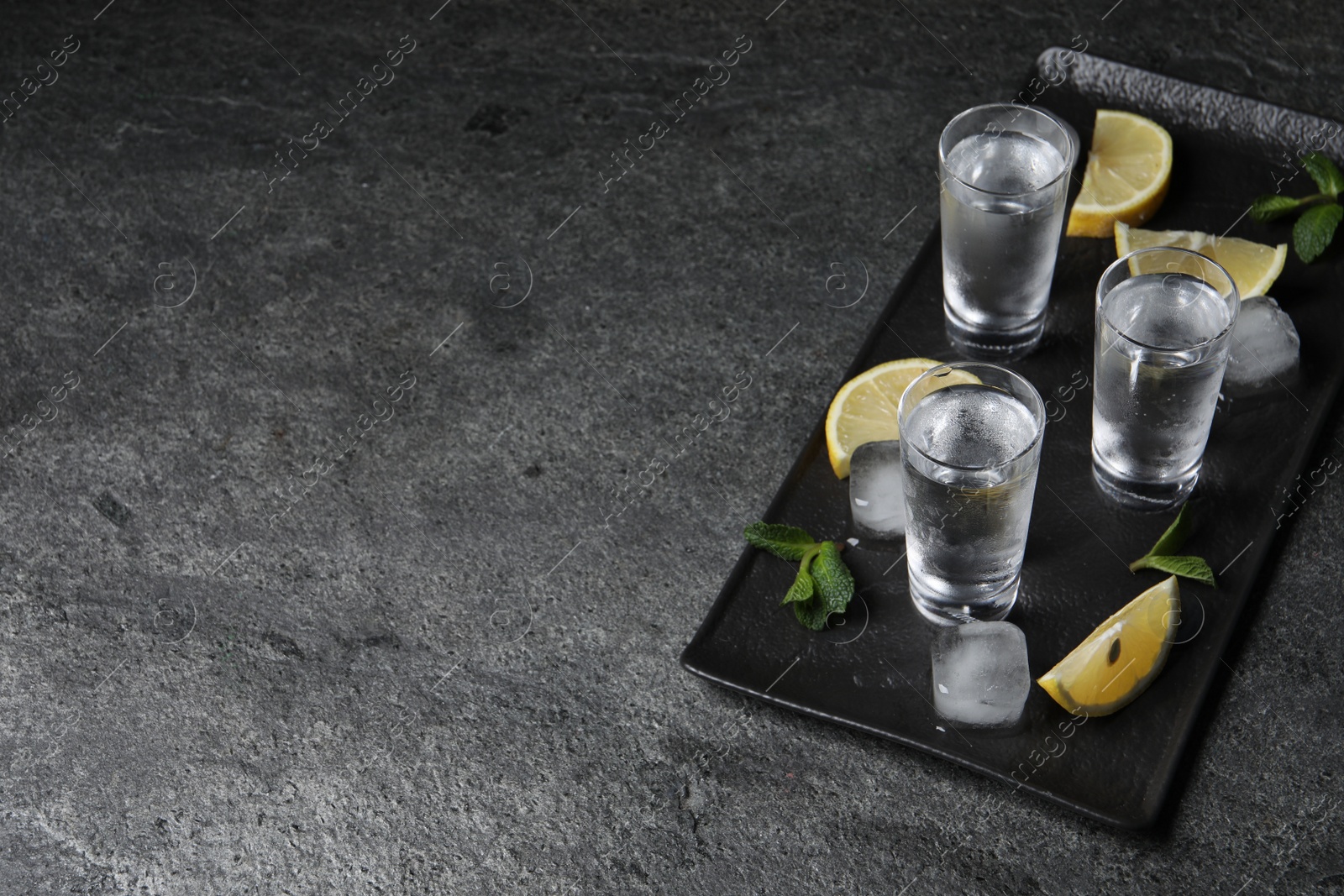 Photo of Shot glasses of vodka with lemon slices, mint and ice on grey table. Space for text