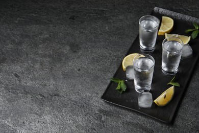 Shot glasses of vodka with lemon slices, mint and ice on grey table. Space for text