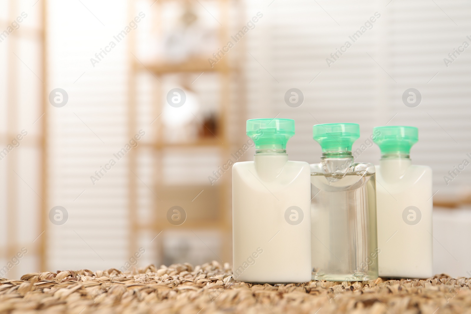 Photo of Mini bottles of cosmetic products on wicker mat against blurred background. Space for text