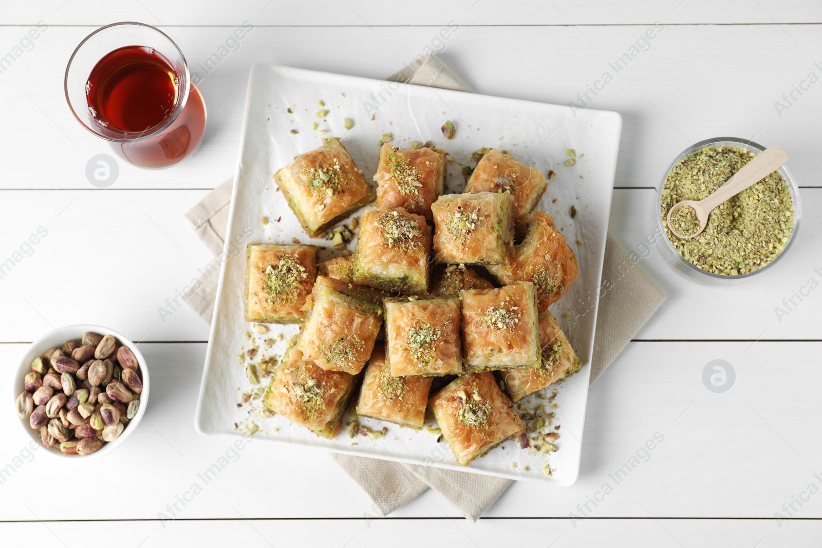 Photo of Delicious fresh baklava with chopped nuts served on white wooden table, flat lay. Eastern sweets