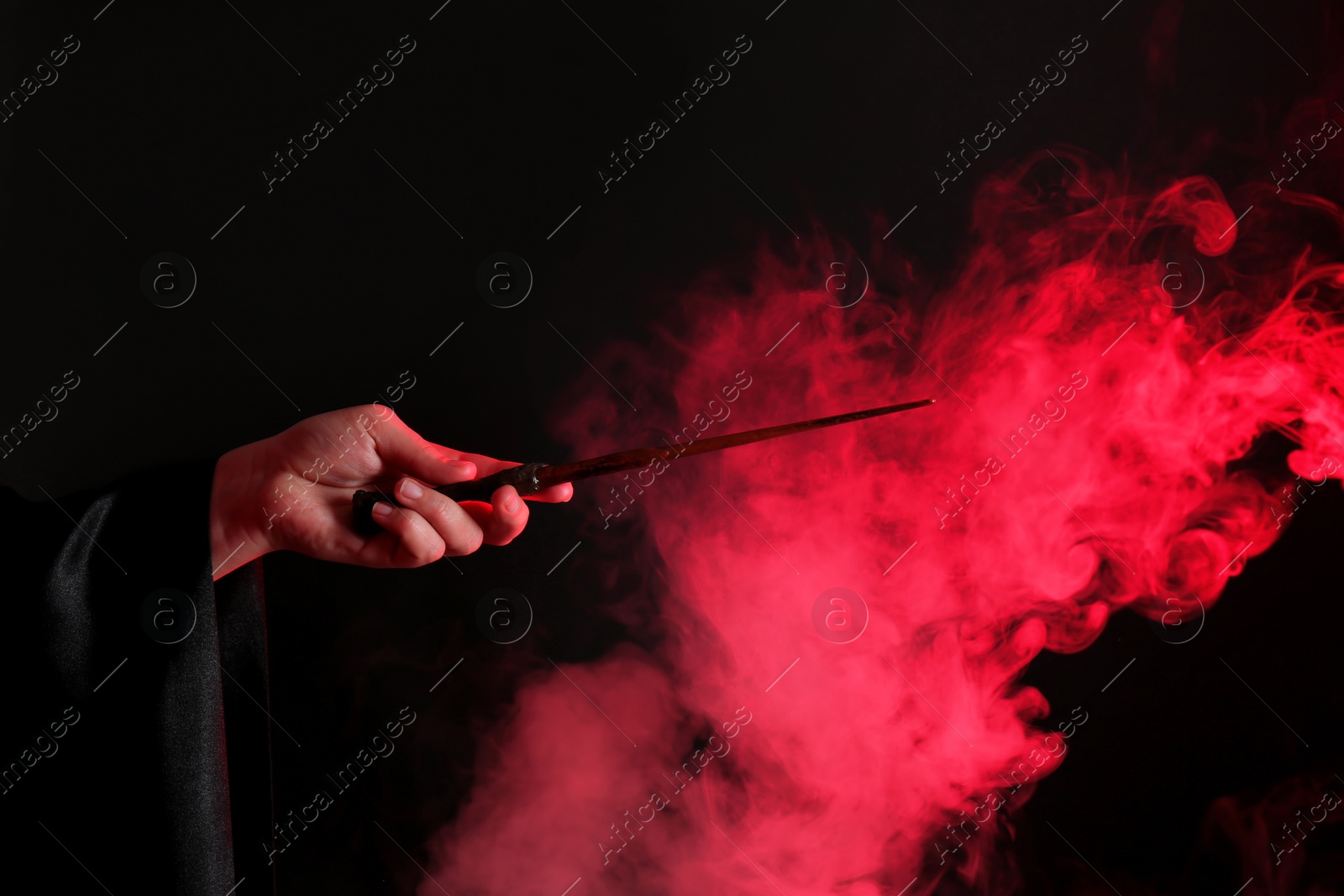 Photo of Magician holding wand in smoke on dark background, closeup