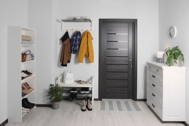 Photo of Beautiful hallway interior with coat rack, chest of drawers and shoe storage bench near wooden door