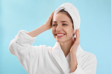 Photo of Beautiful young woman with hair wrapped in towel after washing on light blue background
