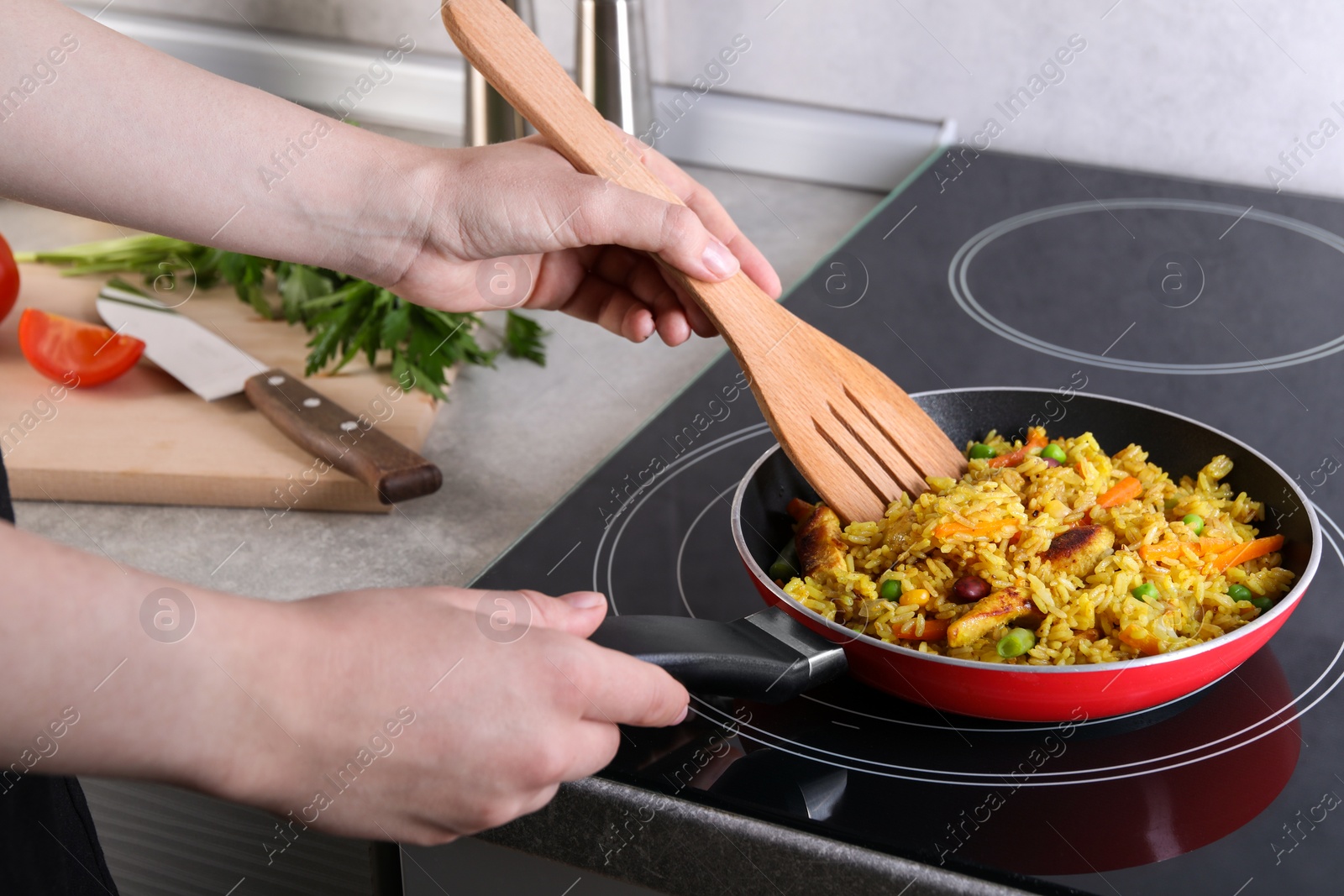 Photo of Woman frying rice with meat and vegetables on induction stove in kitchen, closeup