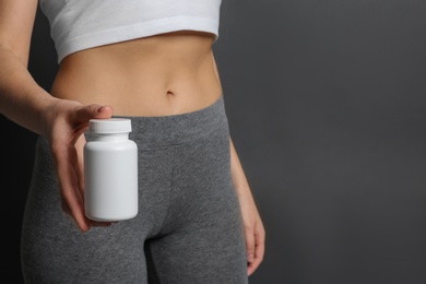 Photo of Slim woman holding bottle of weight loss pills against gray background, closeup. Space for text