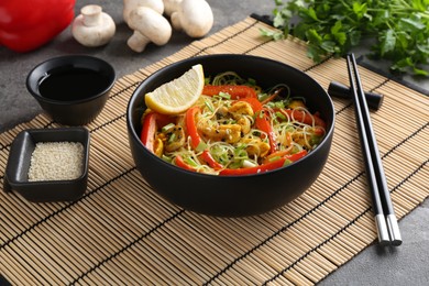 Photo of Stir-fry. Delicious cooked noodles with chicken and vegetables in bowl served on gray textured table