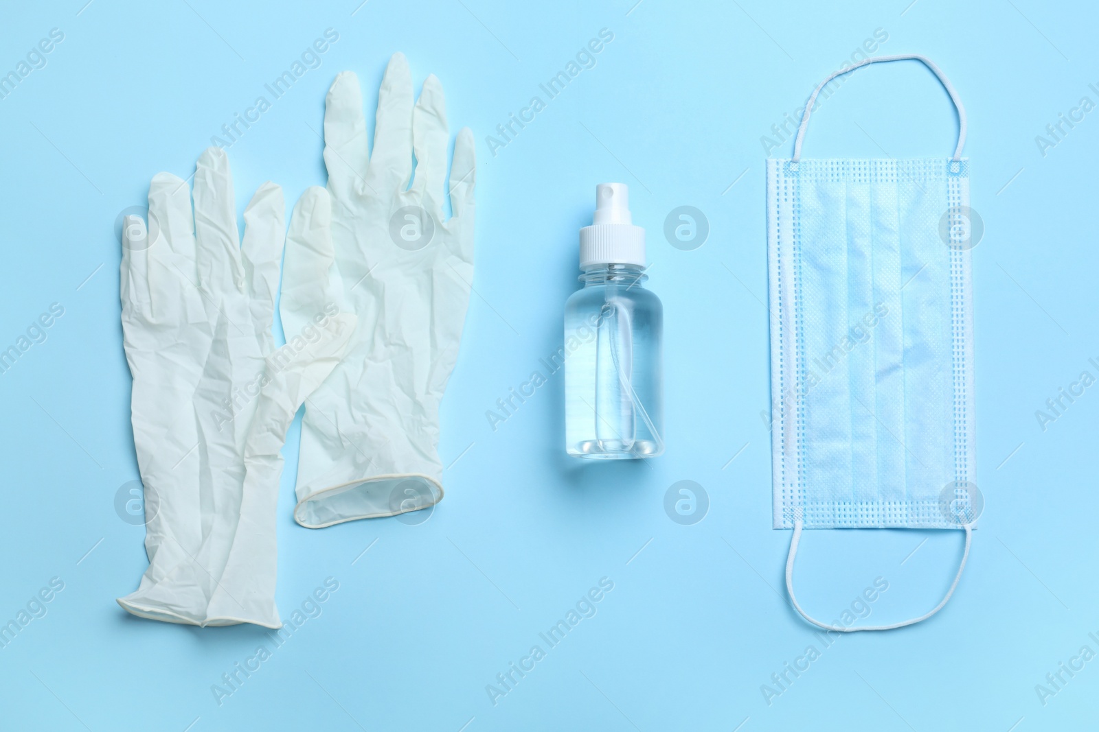 Photo of Medical gloves, mask and hand sanitizer on light blue background, flat lay