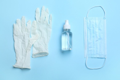 Photo of Medical gloves, mask and hand sanitizer on light blue background, flat lay