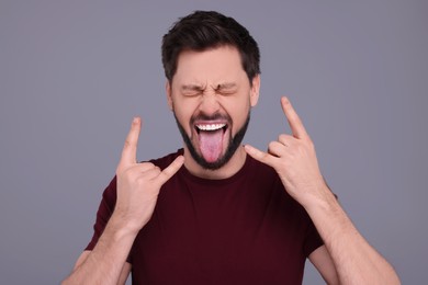 Photo of Happy man showing his tongue and making rock gesture on light grey background