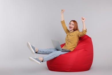 Photo of Happy young woman with laptop sitting on beanbag chair against grey background, space for text
