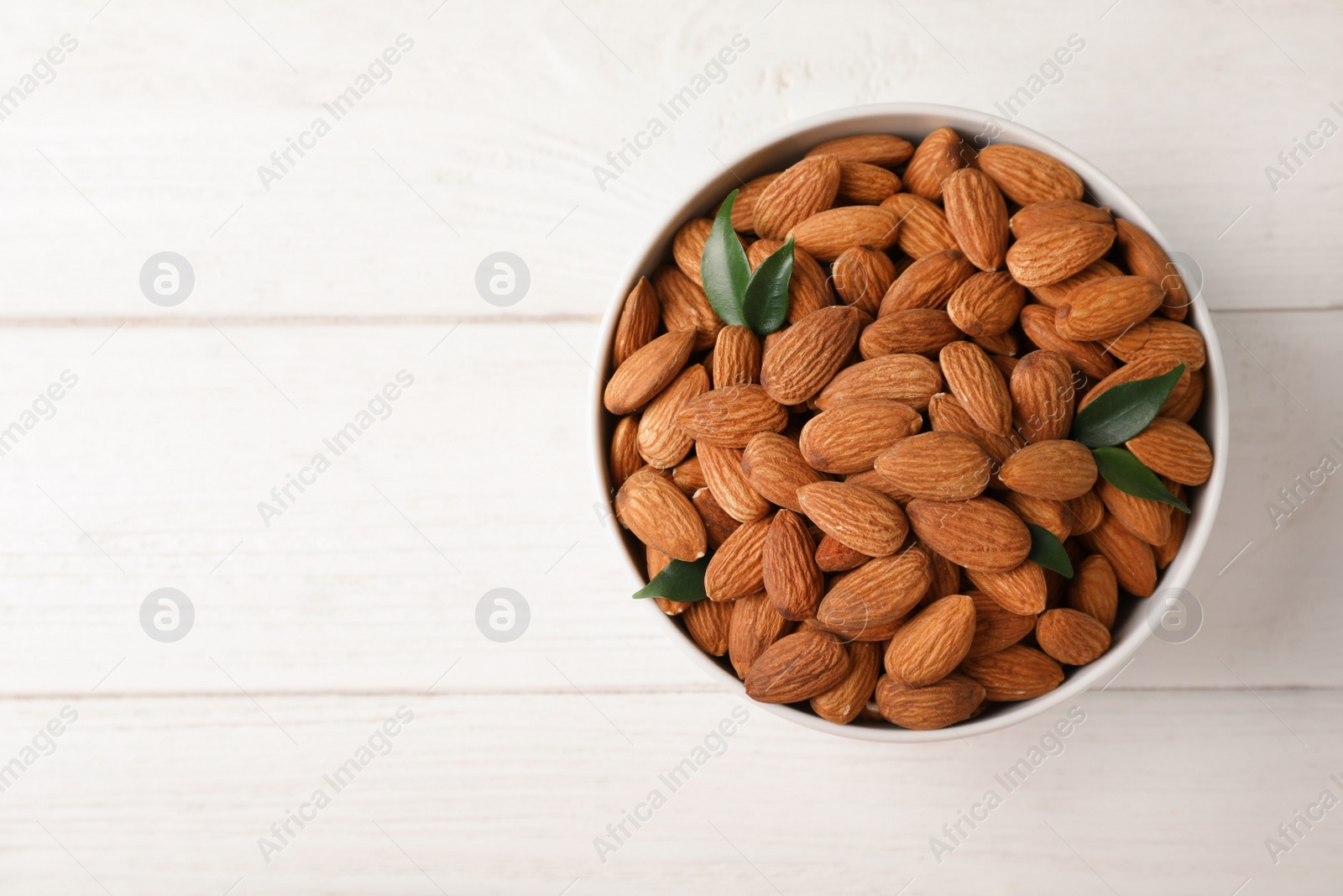 Photo of Tasty organic almond nuts in bowl and space for text on table, top view